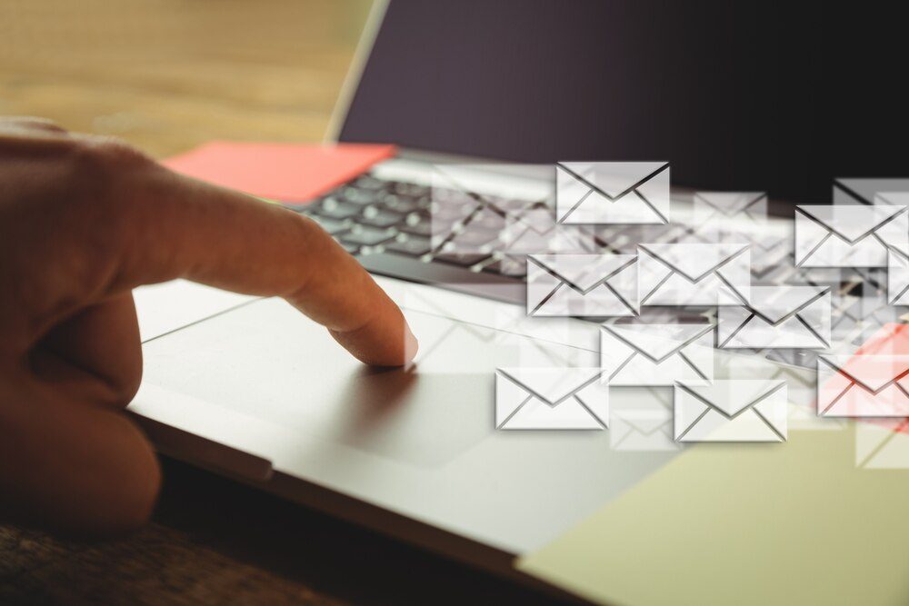 Mano tocando un portátil rodeado de sobres de correo electrónico